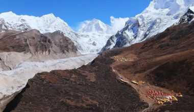 A stunning mountain scenery with a base camp built on dry ground and snowy peaks around.