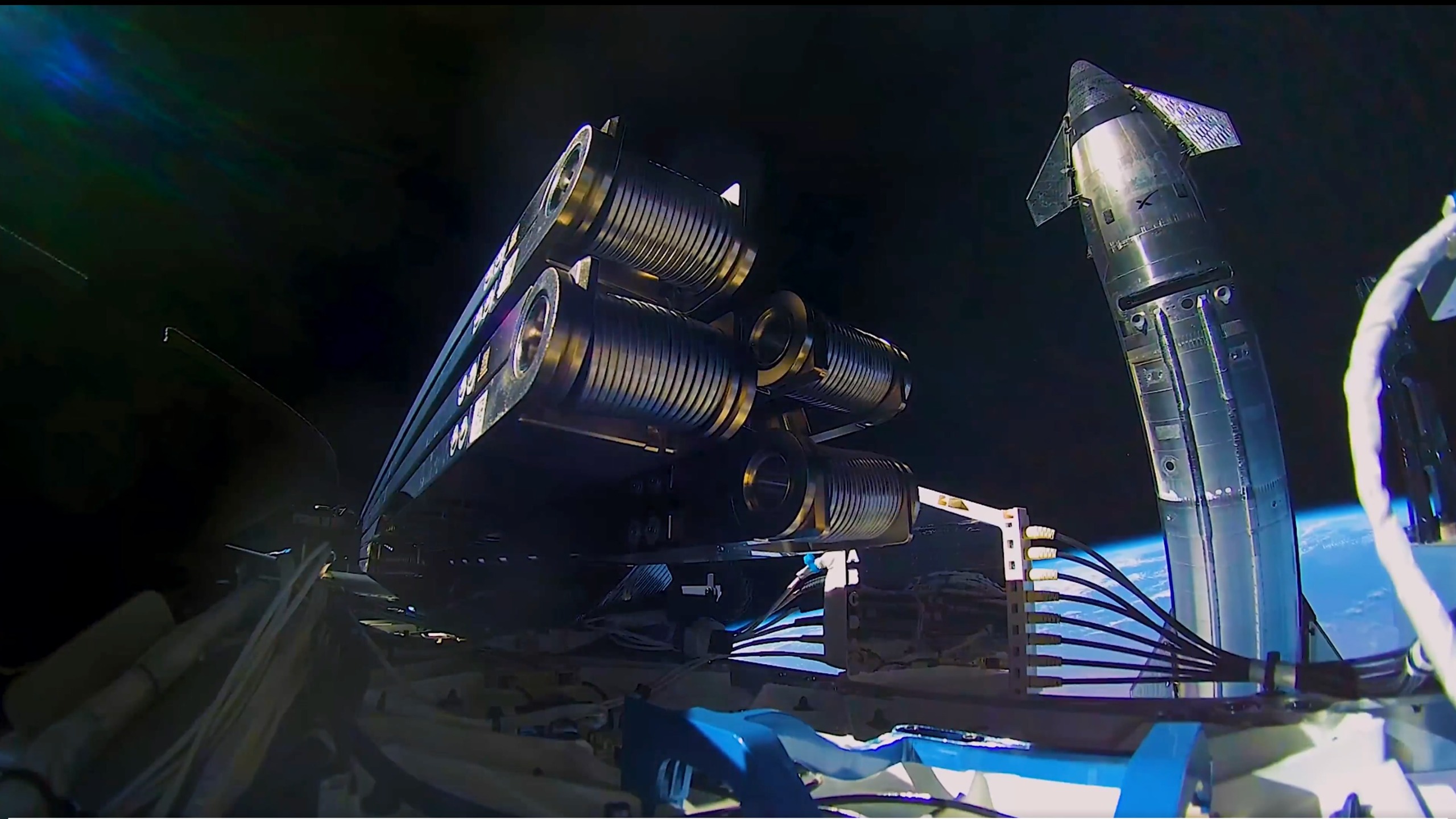 a large silver spacecraft is seen in orbit with earth in the background, in a photo taken by a nearby satellite, parts of which are visible in the foreground