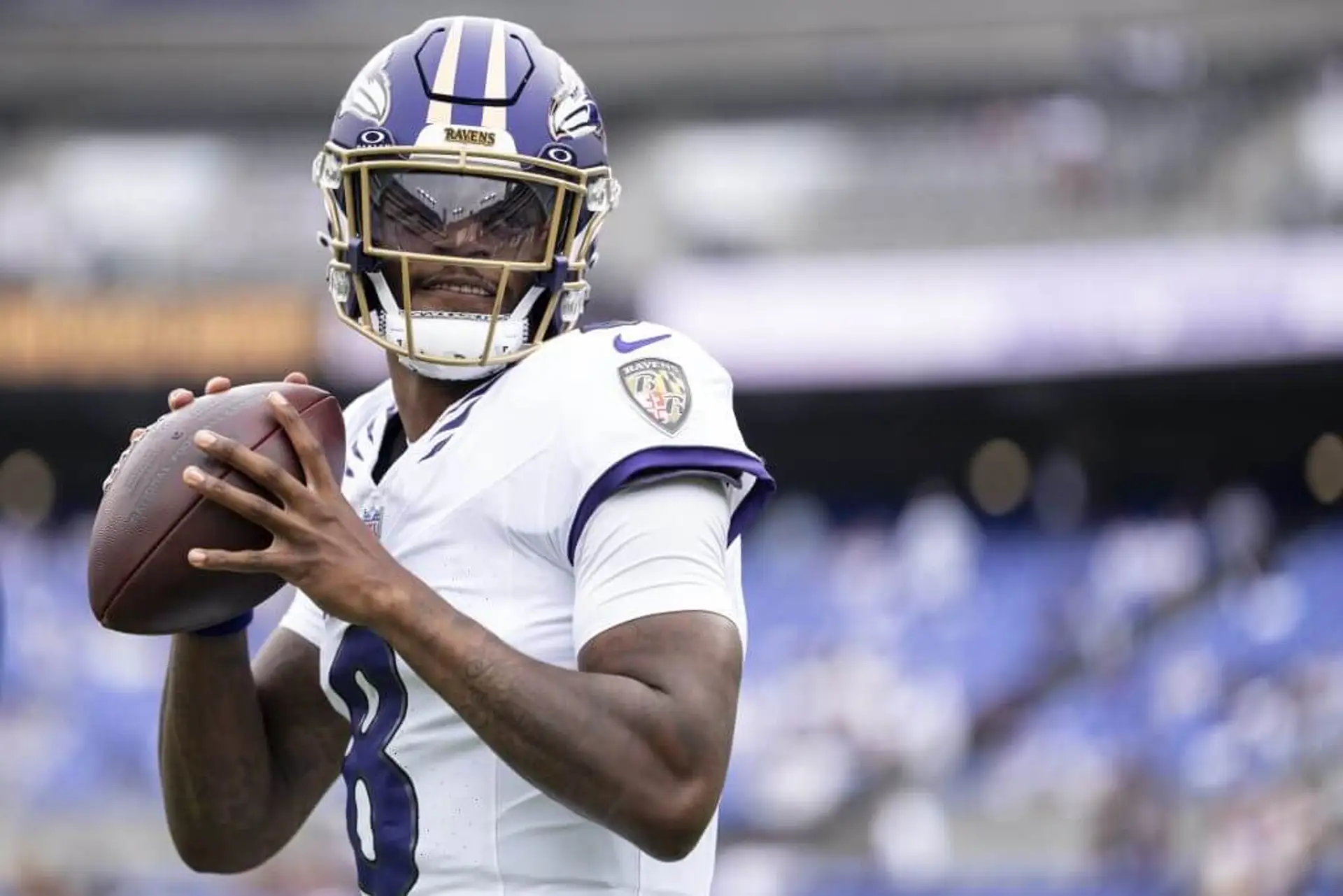 Quarterback in purple helmet and white jersey looks to throw the ball.