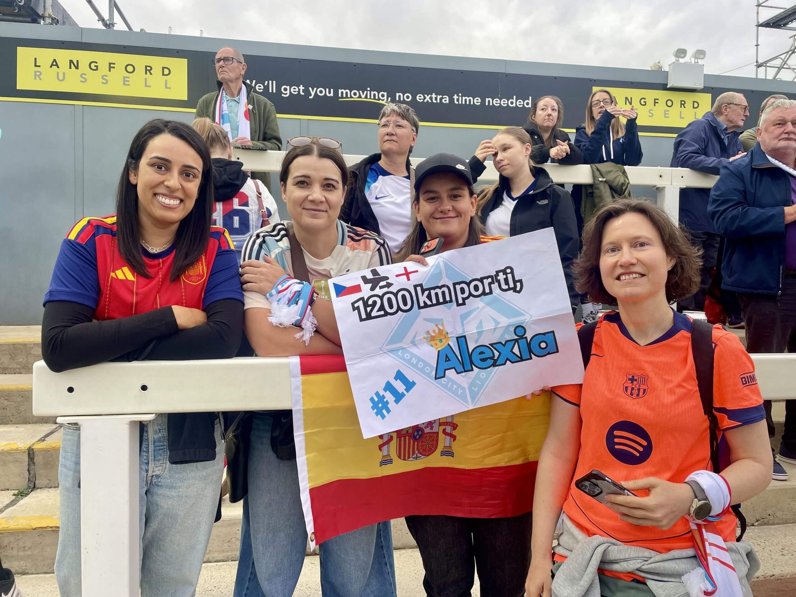 Fans pose at a London City Lionesses game, holding up a sign in tribute to Alexia Putellas