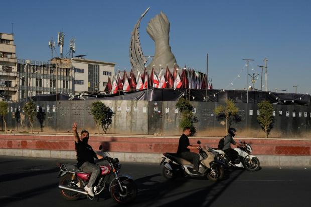 Men drive by a monument depicting the clenched fist of the Supreme Leader Ayatollah Ali Khamenei.