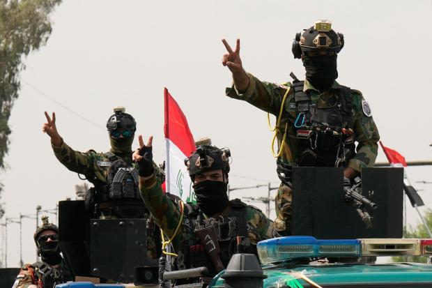 Iraqi security officers flash victory signs while riding in vehicles decorated with national flags.