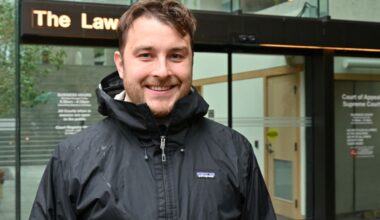 A light skinned man wearing a dark-coloured rain jacket smiles at the camera.