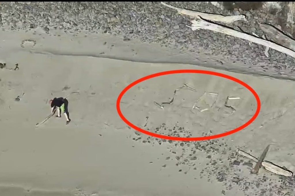 Aerial view of a person drawing "SOS" in the sand on a beach.
