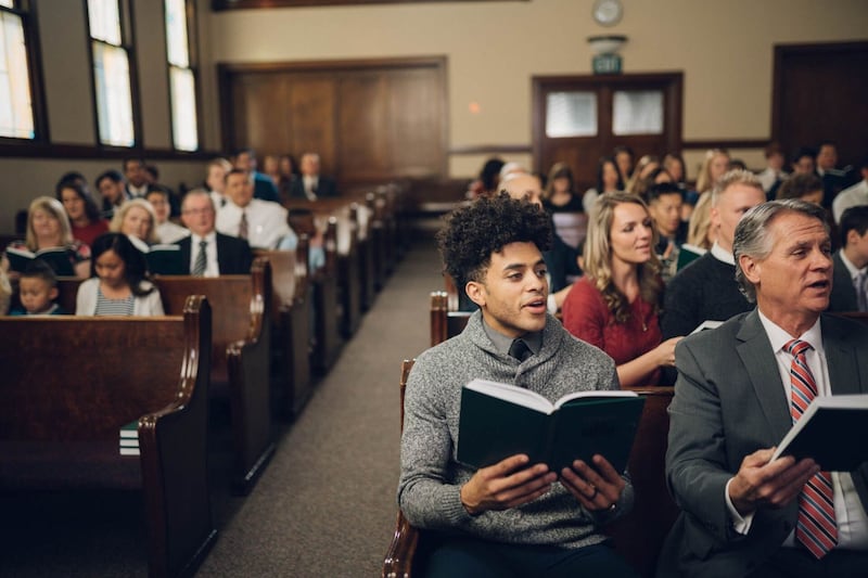 A group of people singing hymns during a sacrament meeting inside a chapel.