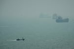 A motorboat travels past commercial vessels anchored amid haze in the Strait of Hormuz off Bandar Abbas, Iran, Monday, Sept. 7, 2026.