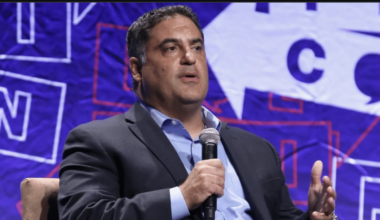 Cenk Uygur speaks into a handheld microphone during an onstage discussion.