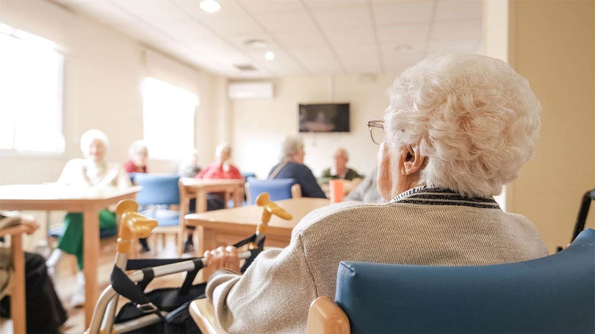 Elderly woman seated with a walker at a nursing home.