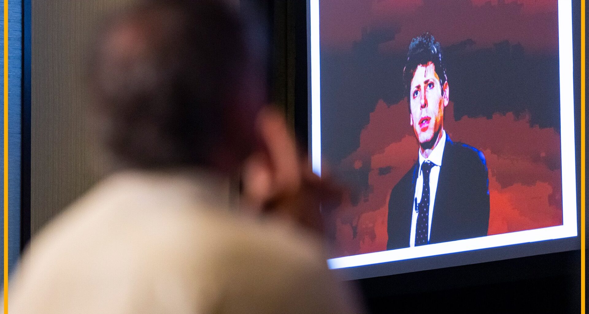 A man looks at a presentation with a man in front of a red background