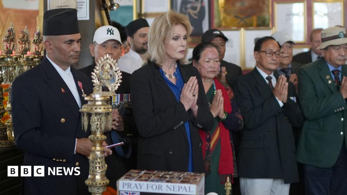 A woman with long, light hair stands with her hands together as though in prayer. She stands in a row of men and women of Nepalese appearance, many with their hands together.