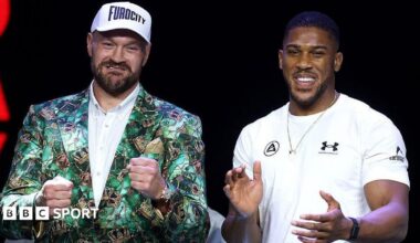 Tyson Fury holds up his fists and Anthony Joshua holds up his hands and smiles