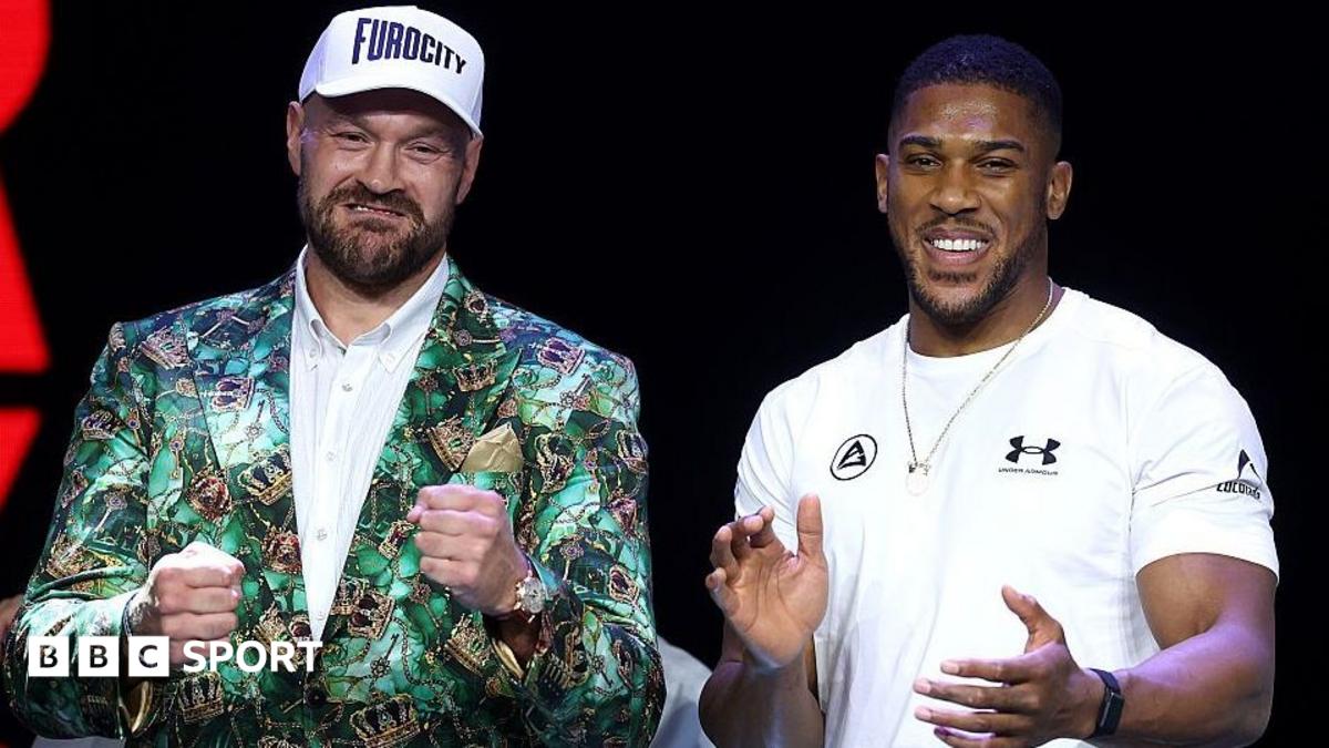 Tyson Fury holds up his fists and Anthony Joshua holds up his hands and smiles