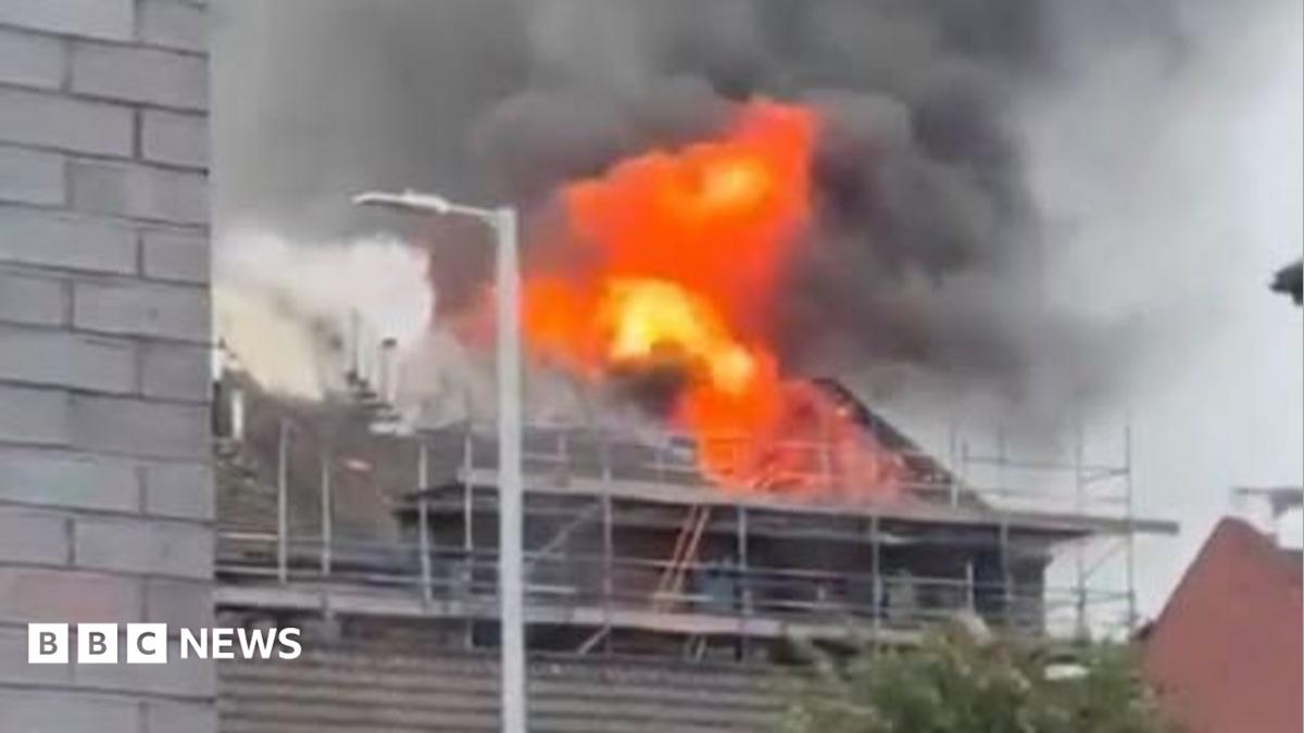 A building covered in scaffolding with flames emerging from the roof.