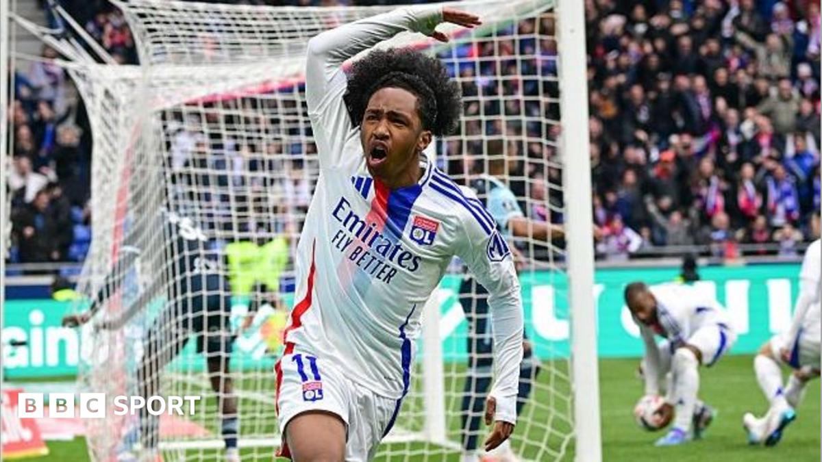 Malick Fofana, wearing Lyon's white kit with a red-and-blue stripe, celebrates scoring a goal by waving his right arm in the air