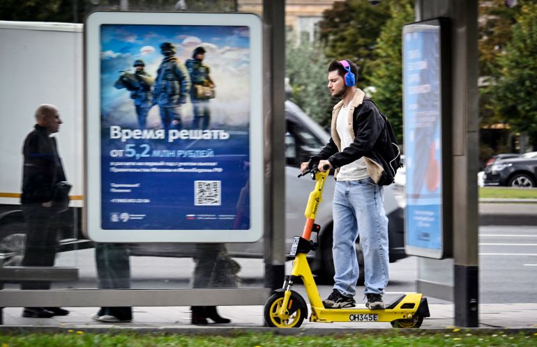 A man on a scooter rolls past a billboard promoting contract army service, offering 5 200 000 rubles for the first year of the contract (about USD 61 800), and reading "Time to Decide" in western Moscow on September 21, 2026.