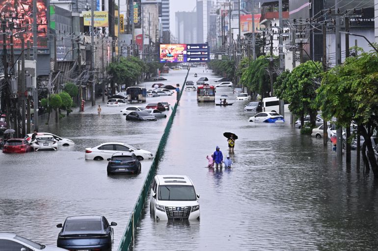 People walk past abandoned vehicles on a flooded Petchaburi road in Bangkok on September 26, 2026.