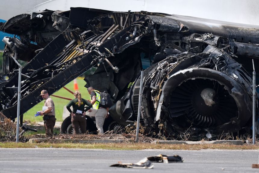 Authorities stand near a destroyed wing and engine Tuesday as they work the scene of Sunday's Amazon cargo plane crash.