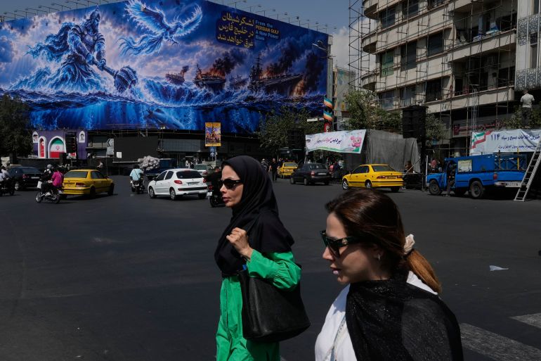 Pedestrian walk past a billboard depicting a Persian legendary hero and flying figure hitting U.S. aircraft carriers alongside the message in English and Farsi: "From the Persian Gulf a new power rises" "The army of Satan will be drowned in the Persian Gulf, " at Islamic Revolution square in downtown Tehran, Iran, Monday, Sept. 14, 2026. (AP Photo/Vahid Salemi)