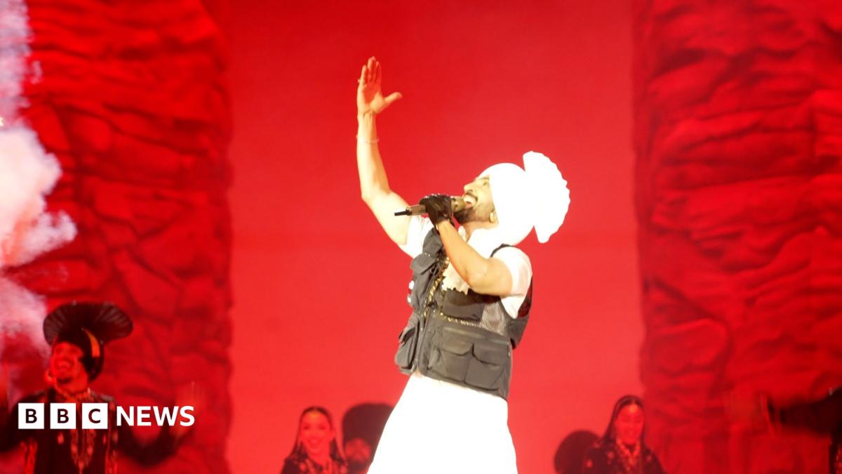Diljit Dosanjh performing at Wembley Stadium against a red backdrop