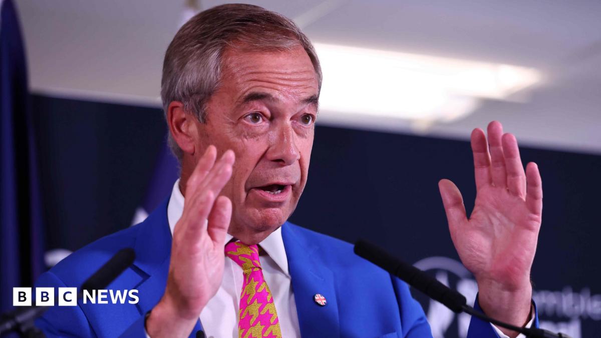Nigel Farage speaking in front of two microphones, wearing a blue suit and a pink and yellow tie. He is wearing a union flag-patterned badge on his lapel.
