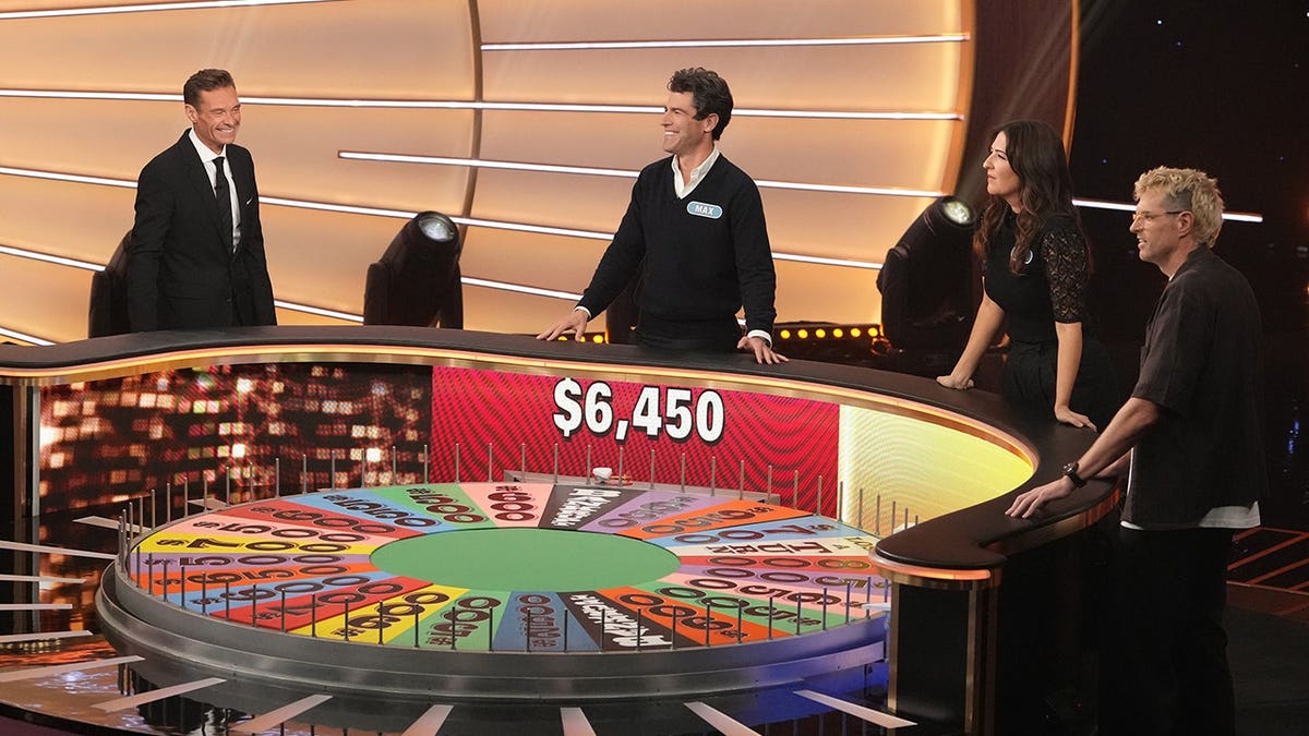 Max Greenfield, D'Arcy Carden and Timothy Simons stand with Ryan Seacrest on the set of Celebrity Wheel of Fortune.