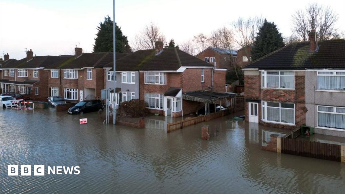 Red brick semi detached homes sit on a street that is completely underwater, with water reaching doorways but below ground floor windows.