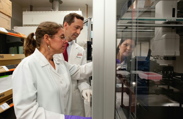 NIAID Vaccine Research Center Lab scientists operating a Biomek Nxp robot within a glass cabinet.