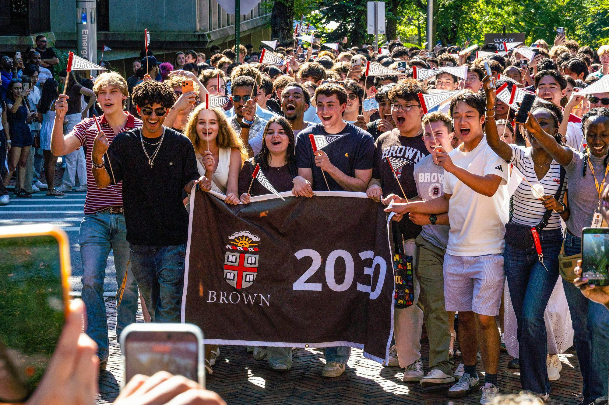 A photo depicts a group of students holding a banner that says 2030, cheering and holding miniature Brown pennants.
