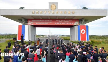 Attendees applaud as North Korea and Russia open their first road bridge, which continues into the distance.