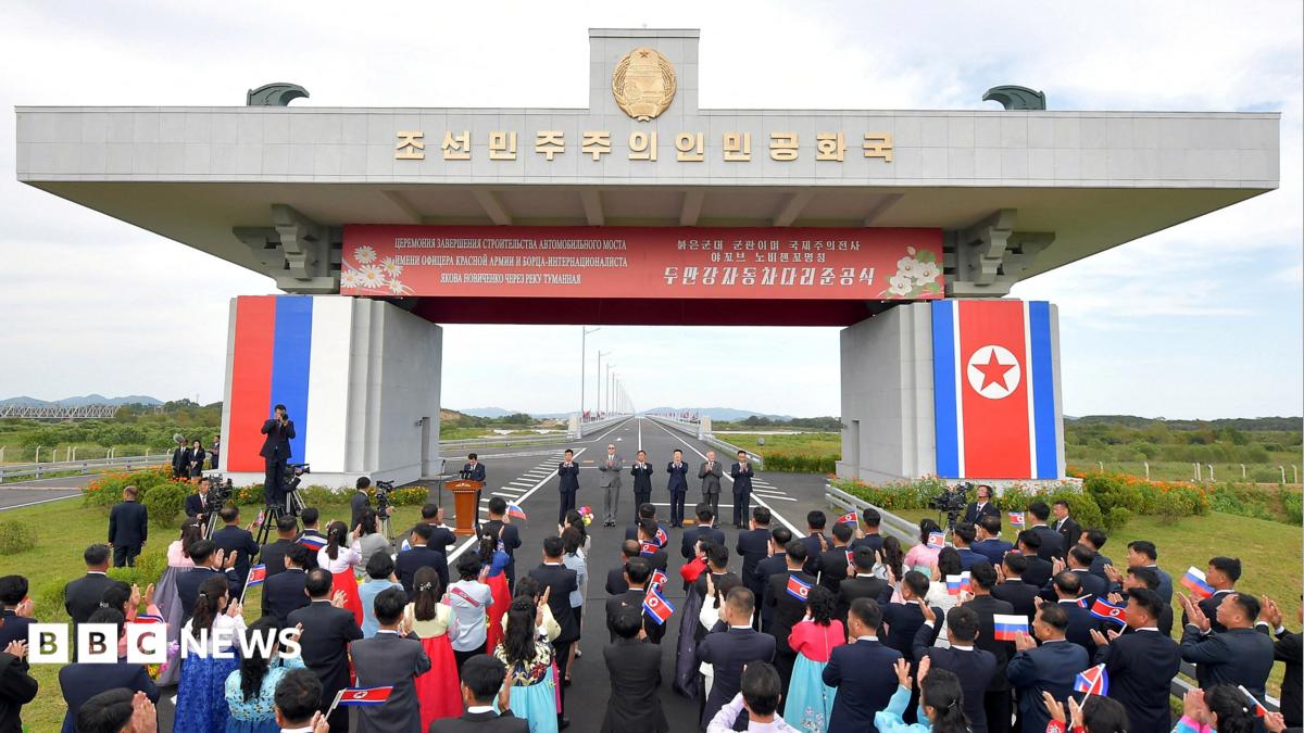 Attendees applaud as North Korea and Russia open their first road bridge, which continues into the distance.