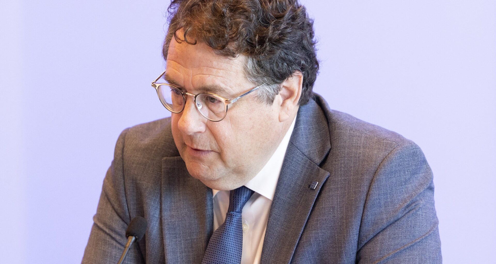 Man sits at table, look downward to the right of him.