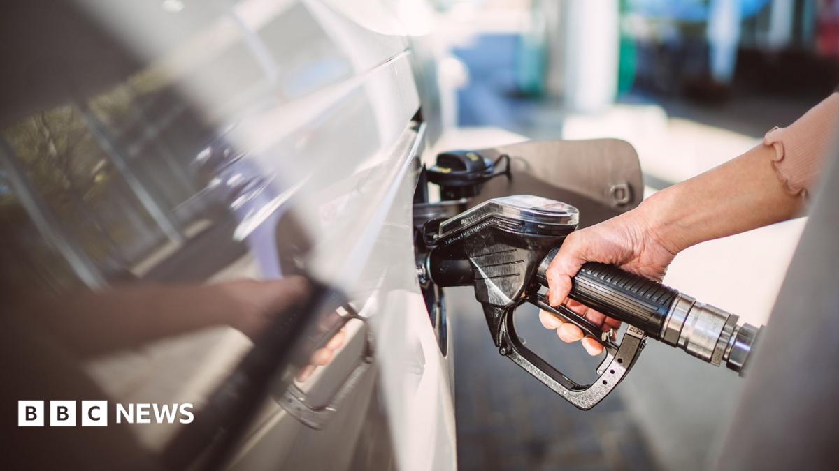 A hand gripping a fuel pump inserted into a white car.