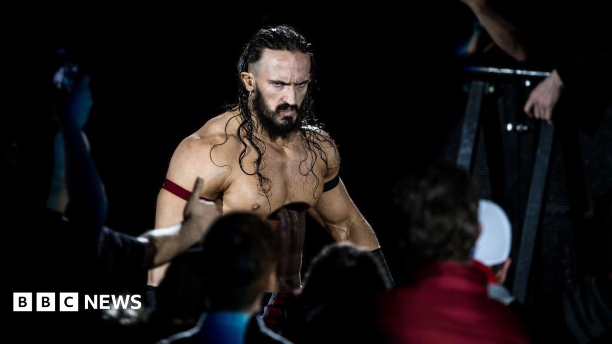 Wrestler Benjamin Satterley arrives at the 2017 WWE Live Duesseldorf. He is shirtless, has long brown hair, a beard and is glowering at the crowd.