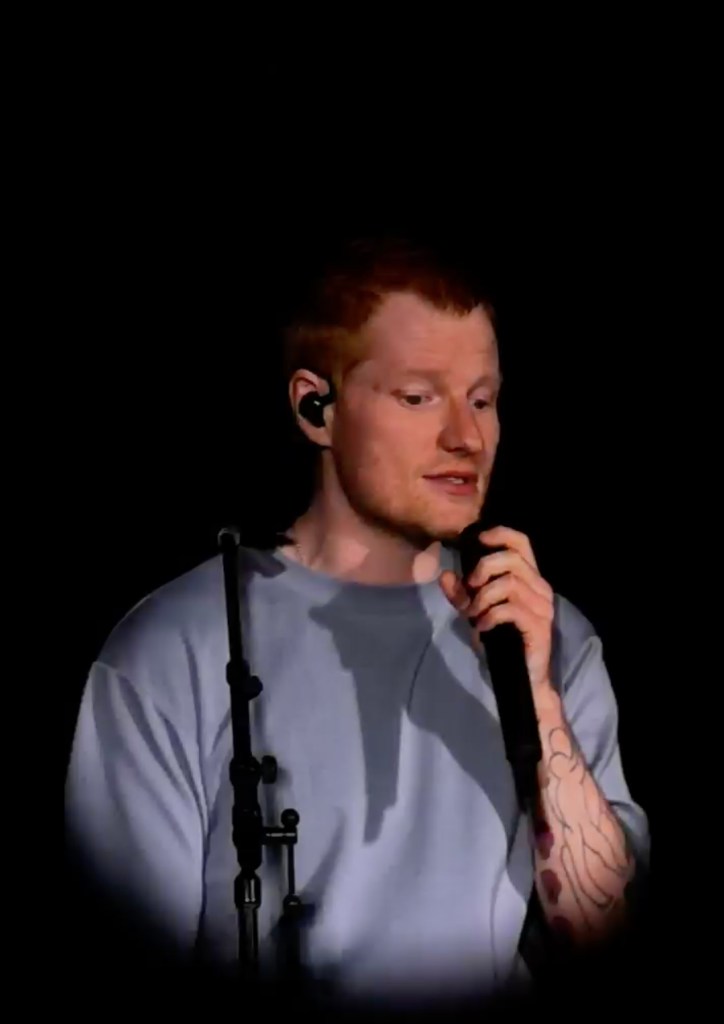 Ed Sheeran singing into a microphone on stage.
