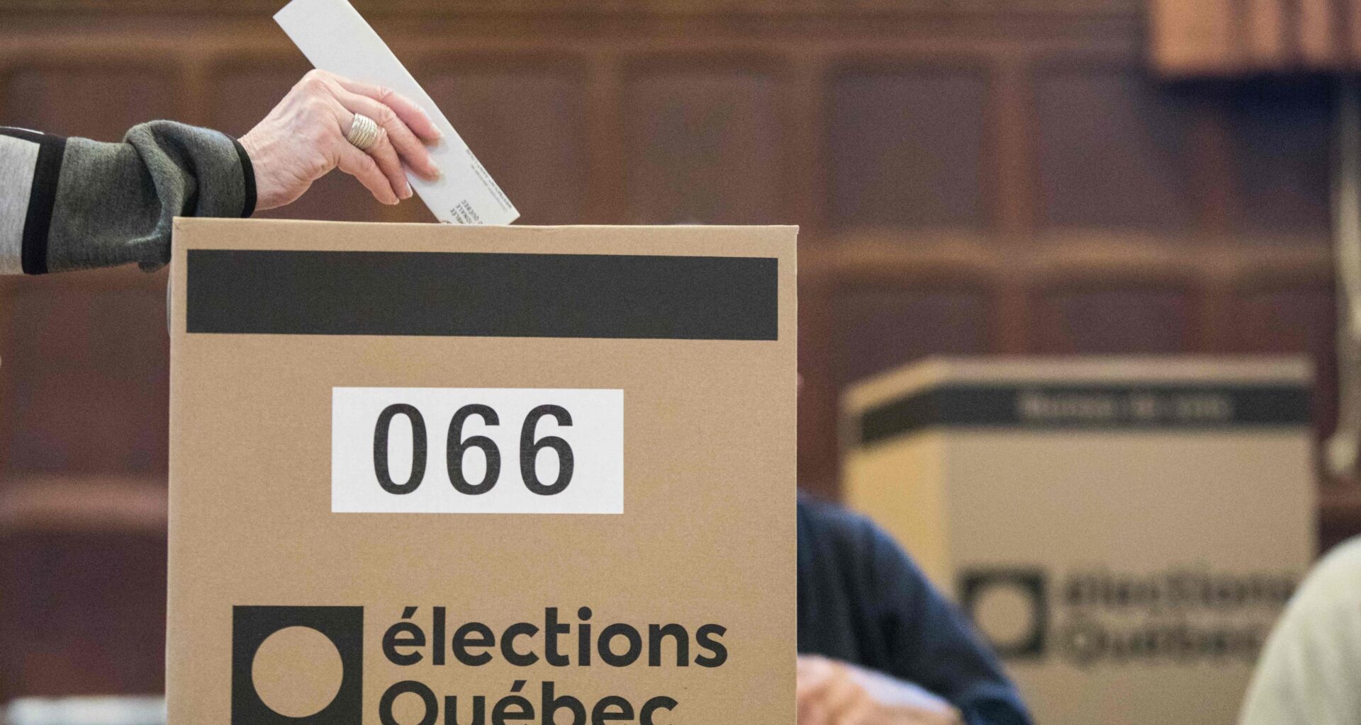 A ballot is dropped into a box with the Élections Québec logo on it.