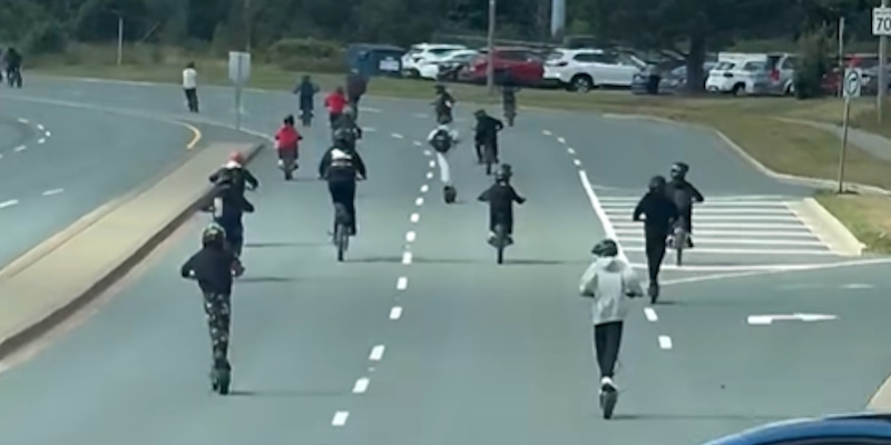 Group of Young People Riding E-Scooters on Busy Roadway Making Rounds Online