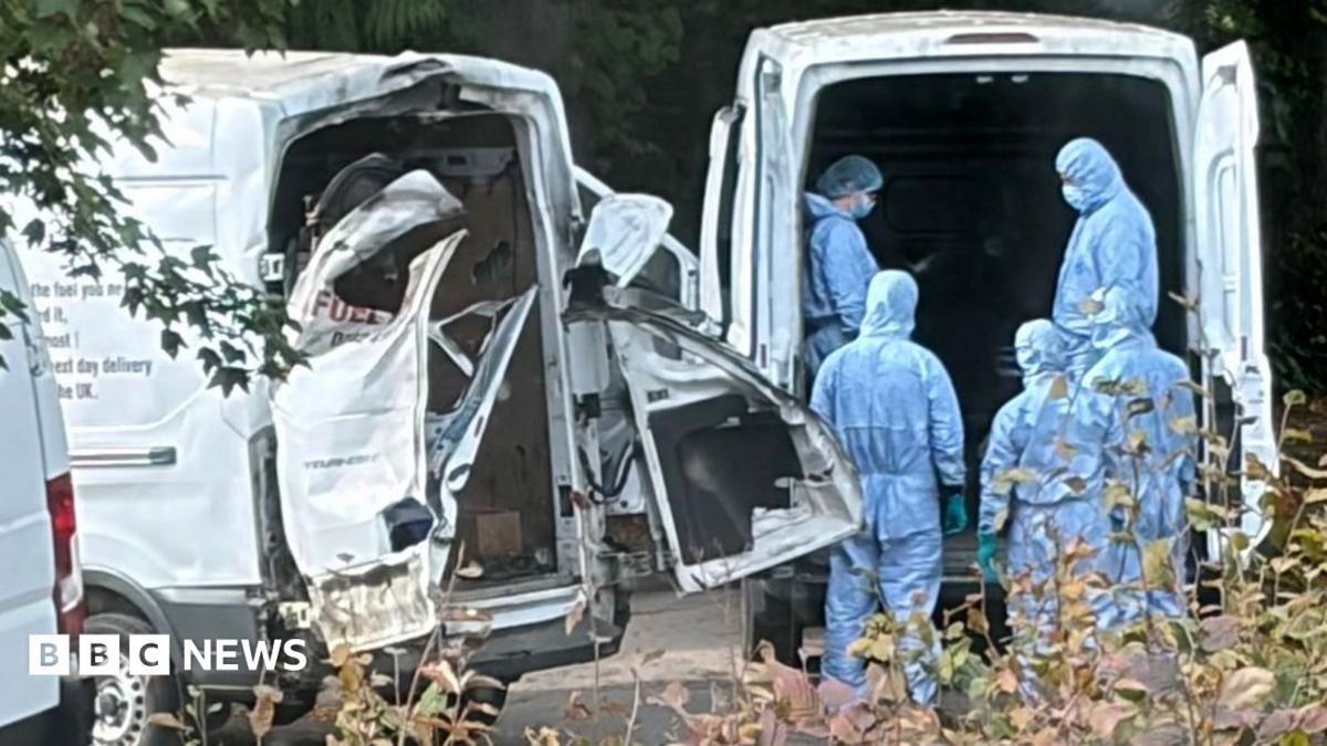 people in blue hazmat suits stand behind a white van next to another white van with the back doors blown off