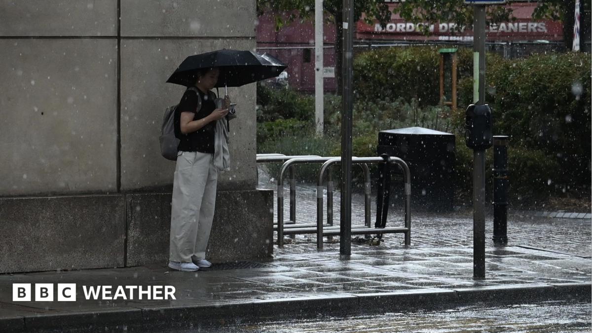 A woman stands with a black umbrella next to a wall in the rain