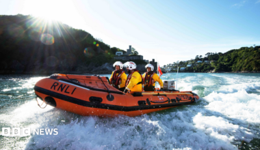 An RNLI boat speeds along the sea coast with three volunteers on board.