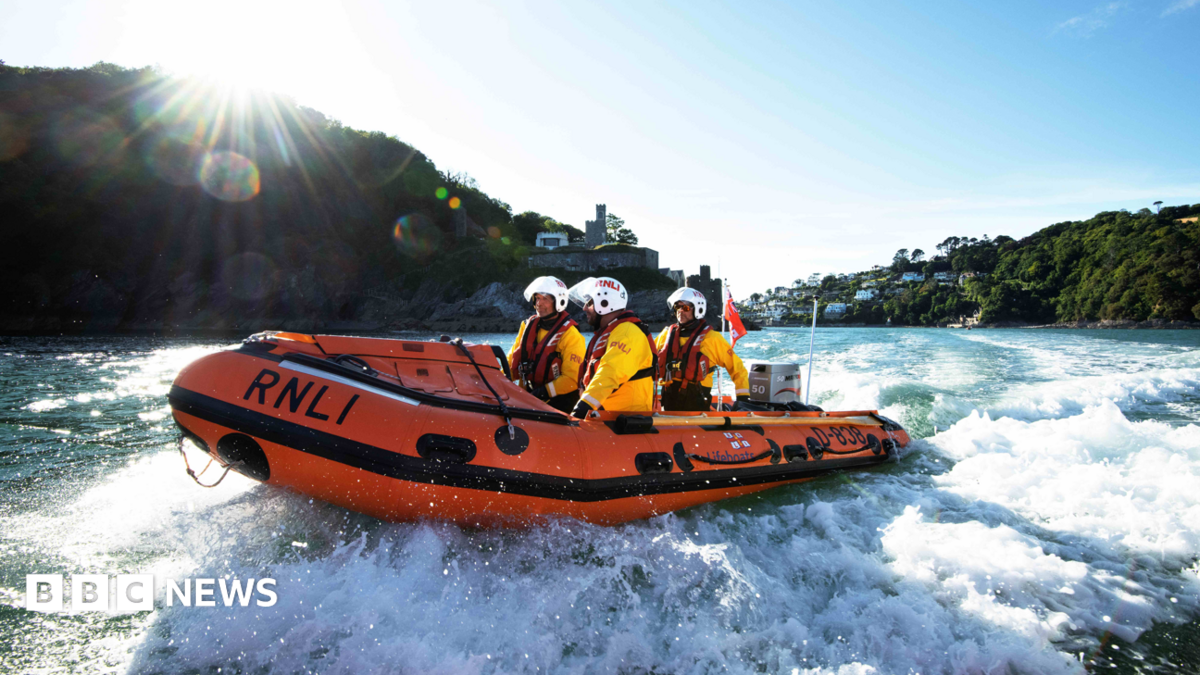 An RNLI boat speeds along the sea coast with three volunteers on board.