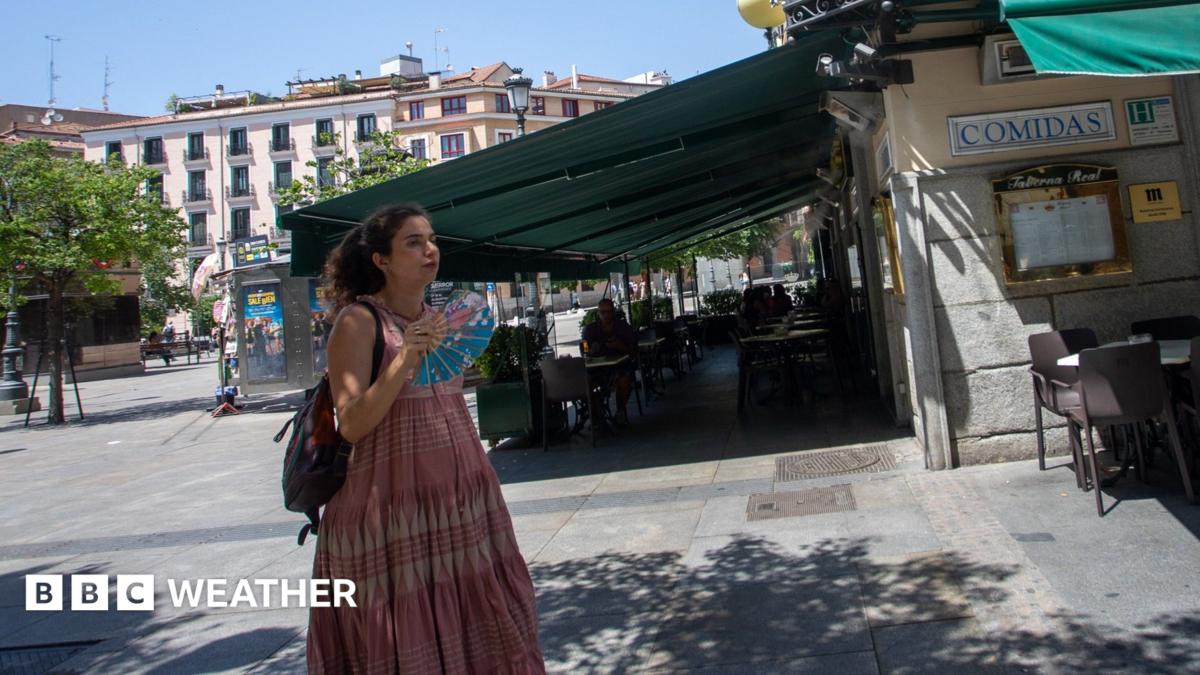 A woman walks through a town square in Madrid, Spain, carrying a handheld fan.