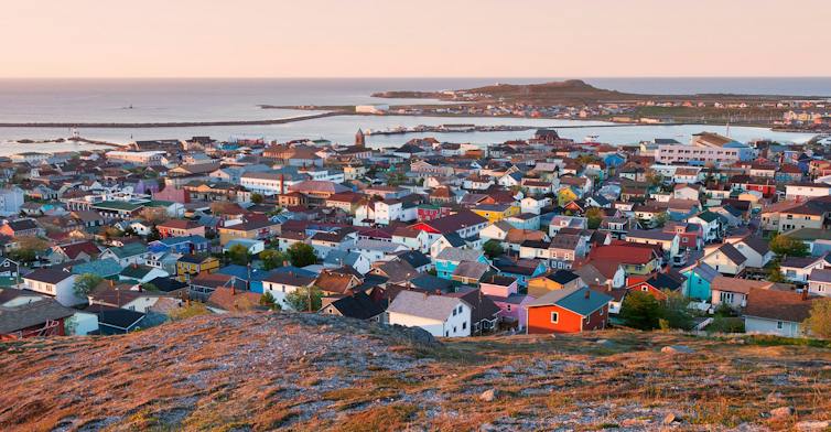 A fishing village of brightly coloured houses at sunrise with the ocean in the background.