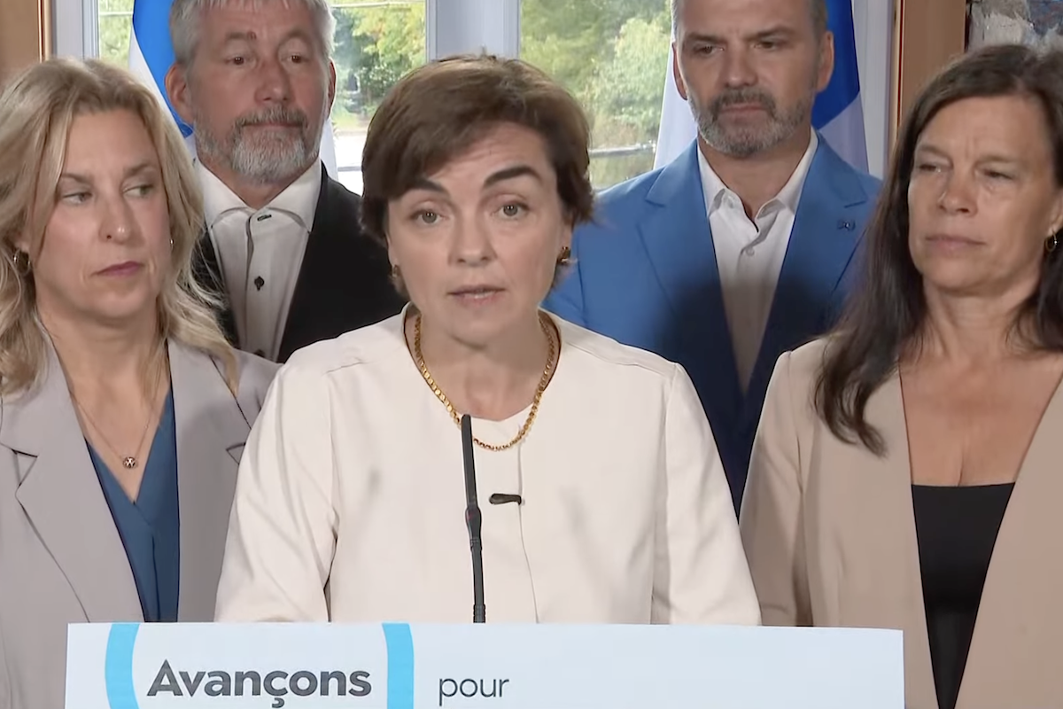 Woman speaks at mic surrounded by people