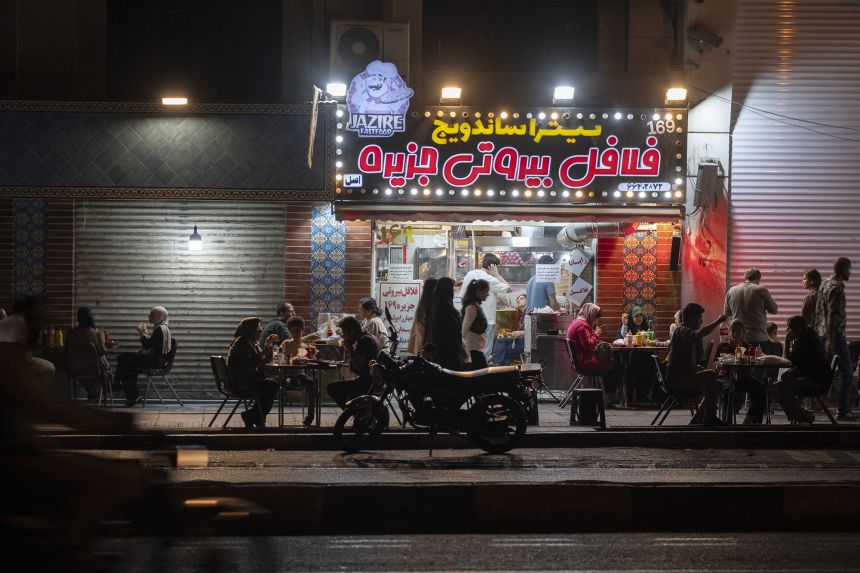 Iranian families eat fast food while sitting along a sidewalk at an outdoor restaurant in downtown Tehran, Iran, on August 30, 2026.