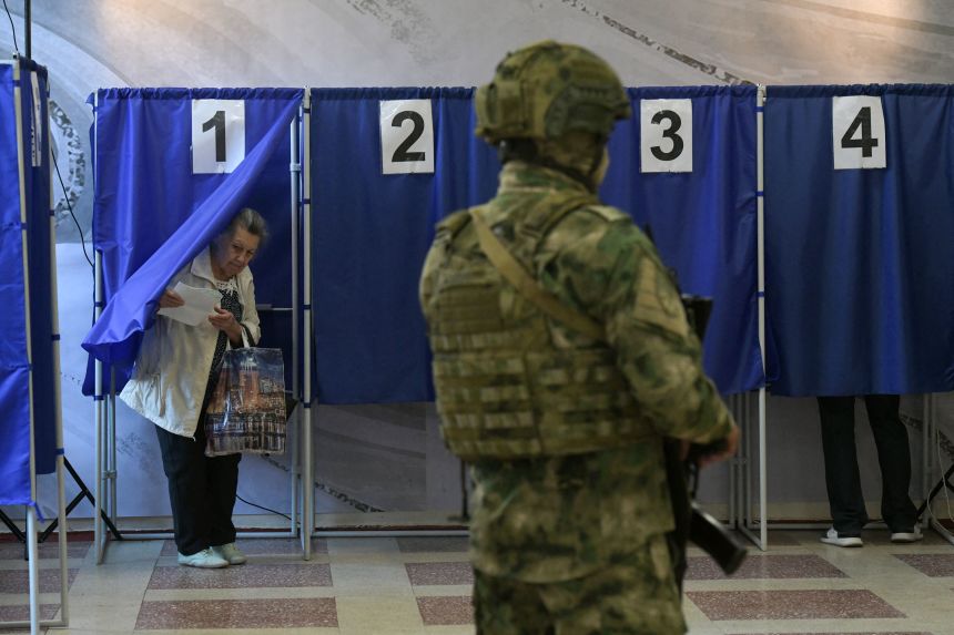 People vote in Russia's parliamentary election as a Russian serviceman secures a polling station in Donetsk, Russian-controlled Ukraine, on September 18.