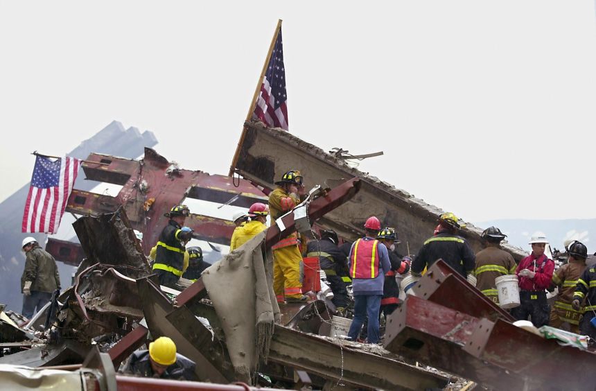 Two American flags fly as firemen, patrolmen and rescuers in red, white, black helmets work side by side at Ground Zero in the early morning September 14, 2001.