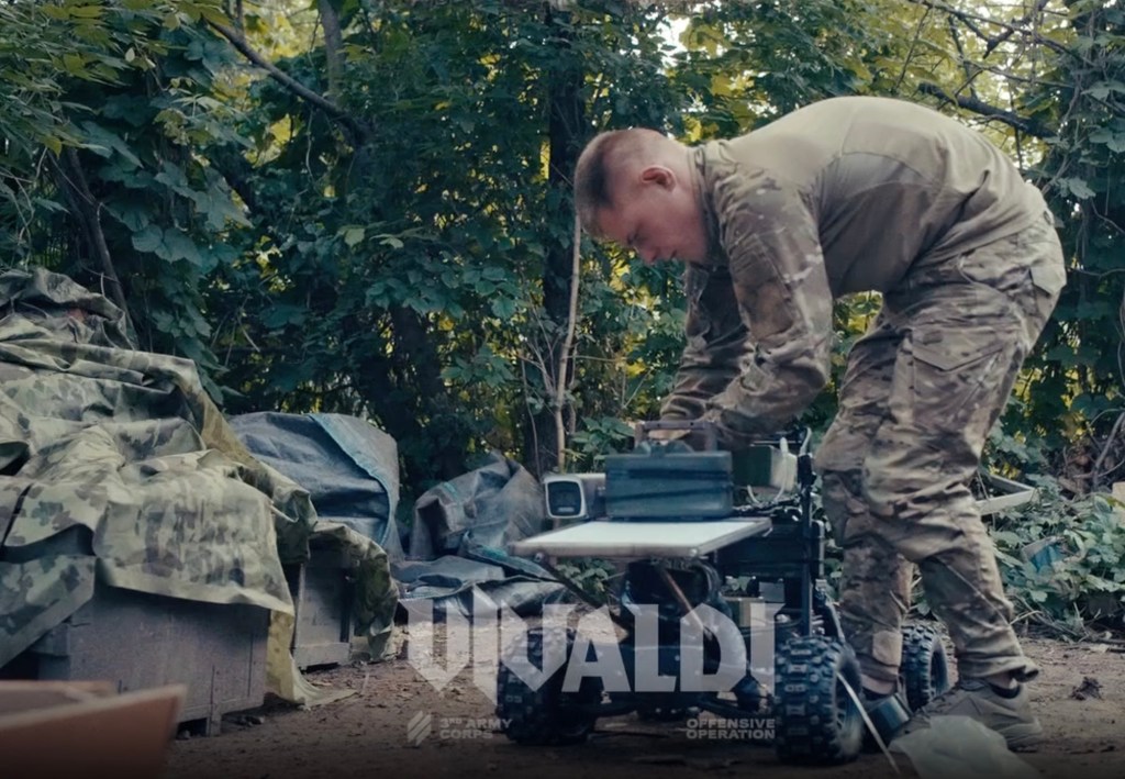 A soldier in camouflage adjusts a kamikaze unmanned ground vehicle.