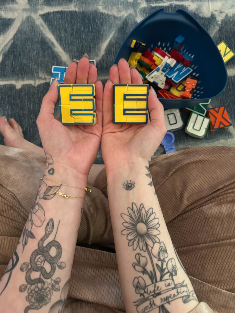In this picture shared by Liz Black, Liz holds her E-letter robot, over four decades old, in her left hand. In her right hand is her son’s E-letter robot. Tattooed along her right arm are the words: “Life is worth repeating.”