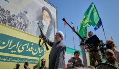 An armed Shiite cleric rides aboard a military vehicle past a billboard depicting Ayatollah Ruhollah Khomeini, founder of the Islamic Republic, during the state-organized "Janfada," or "Sacrifice for Iran," military-style parade in Tehran, Iran, Friday, Sept. 18, 2026. (AP Photo/Vahid Salemi)