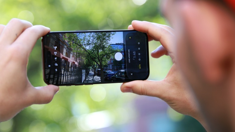 A person holding up an iPhone 18 Pro with the screen facing us. On it is the Camera app and variable aperture settings on the right.